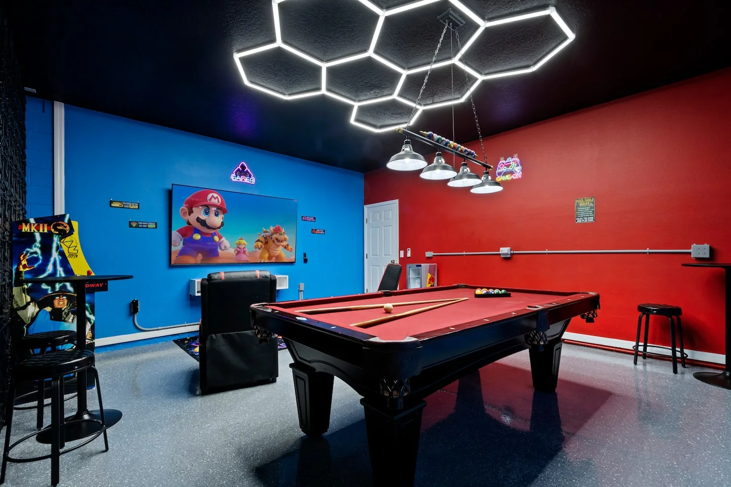 The colorful games room with a red pool table, arcade machines and geometric ceiling lights